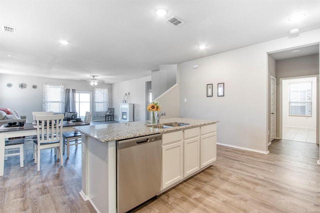 kitchen featuring sink, dishwasher, white cabinetry, light stone countertops, and an island with sink