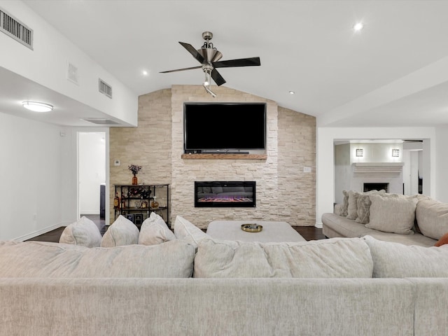 living room featuring ceiling fan, a stone fireplace, vaulted ceiling, and wood-type flooring