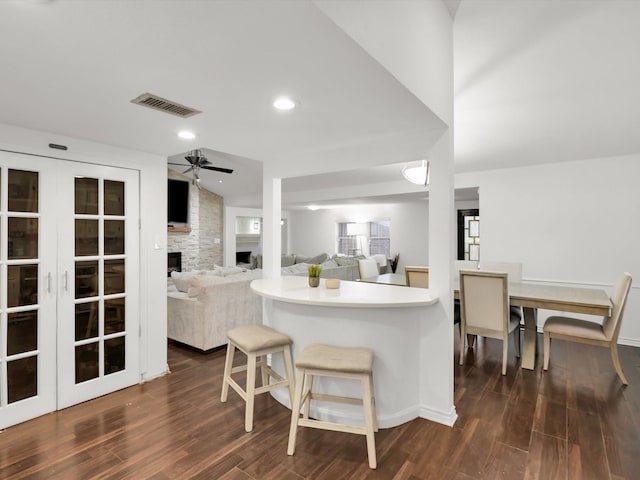 kitchen featuring ceiling fan, dark wood-type flooring, a kitchen bar, and a stone fireplace