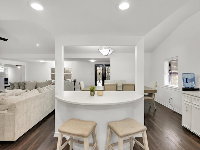 kitchen featuring vaulted ceiling, dark hardwood / wood-style floors, a breakfast bar, and white cabinets