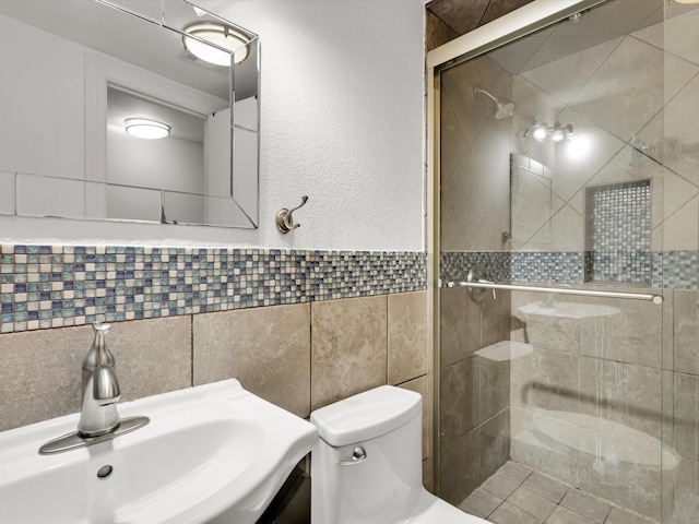 bathroom featuring sink, toilet, tile walls, and a shower with shower door