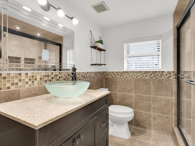 bathroom featuring tile walls, toilet, vanity, and a shower with shower door