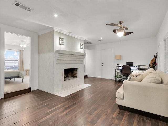 living room featuring ceiling fan, a tiled fireplace, and dark wood-type flooring