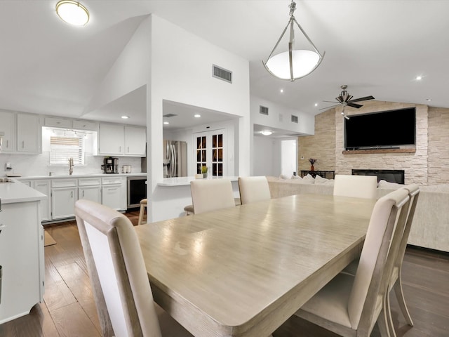 dining room with sink, ceiling fan, dark hardwood / wood-style flooring, a fireplace, and high vaulted ceiling