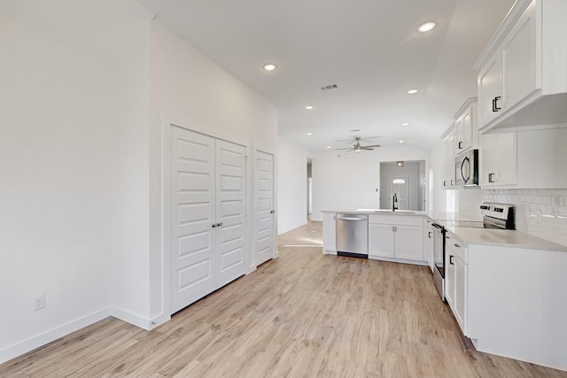 kitchen with kitchen peninsula, stainless steel appliances, ceiling fan, sink, and white cabinets