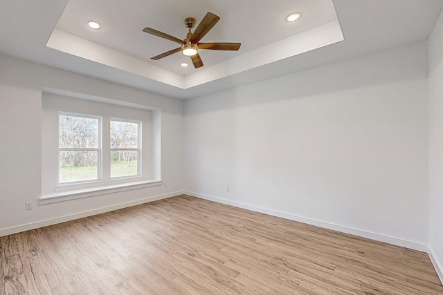 unfurnished room featuring a tray ceiling, ceiling fan, and light hardwood / wood-style floors