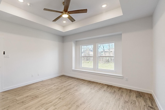 unfurnished room featuring ceiling fan, light hardwood / wood-style floors, and a tray ceiling