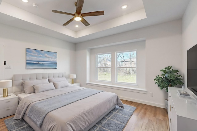 bedroom with ceiling fan, light hardwood / wood-style flooring, and a tray ceiling