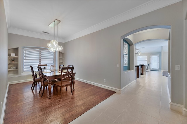 tiled dining space featuring built in features, crown molding, a wealth of natural light, and an inviting chandelier