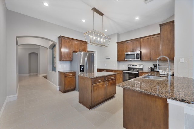 kitchen featuring sink, stainless steel appliances, kitchen peninsula, dark stone counters, and decorative light fixtures