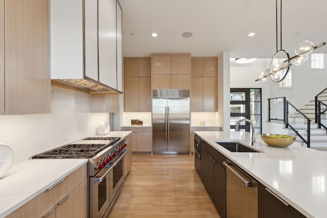 kitchen with high quality appliances, sink, decorative light fixtures, and light brown cabinets