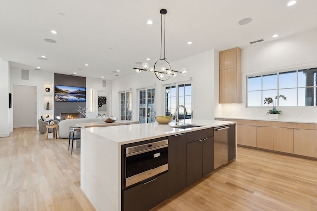 kitchen featuring sink, hanging light fixtures, an island with sink, a large fireplace, and stainless steel appliances