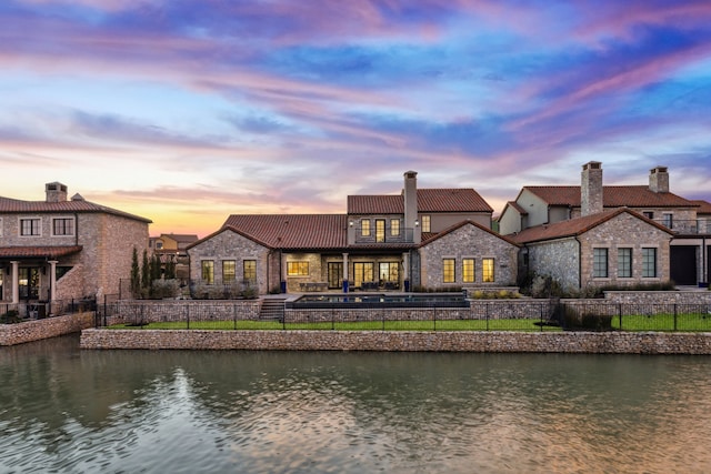 back house at dusk featuring a water view and a balcony