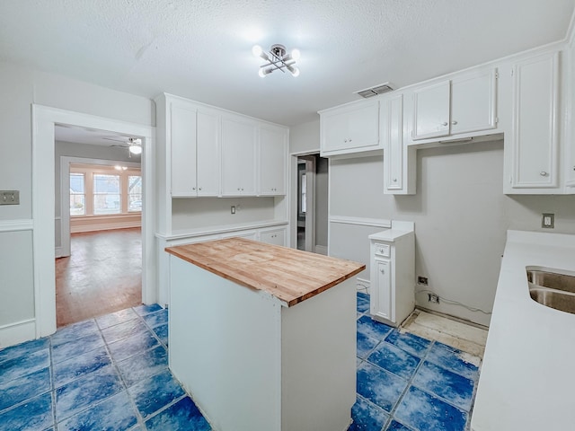 kitchen with a kitchen island, butcher block countertops, a textured ceiling, white cabinets, and ceiling fan with notable chandelier