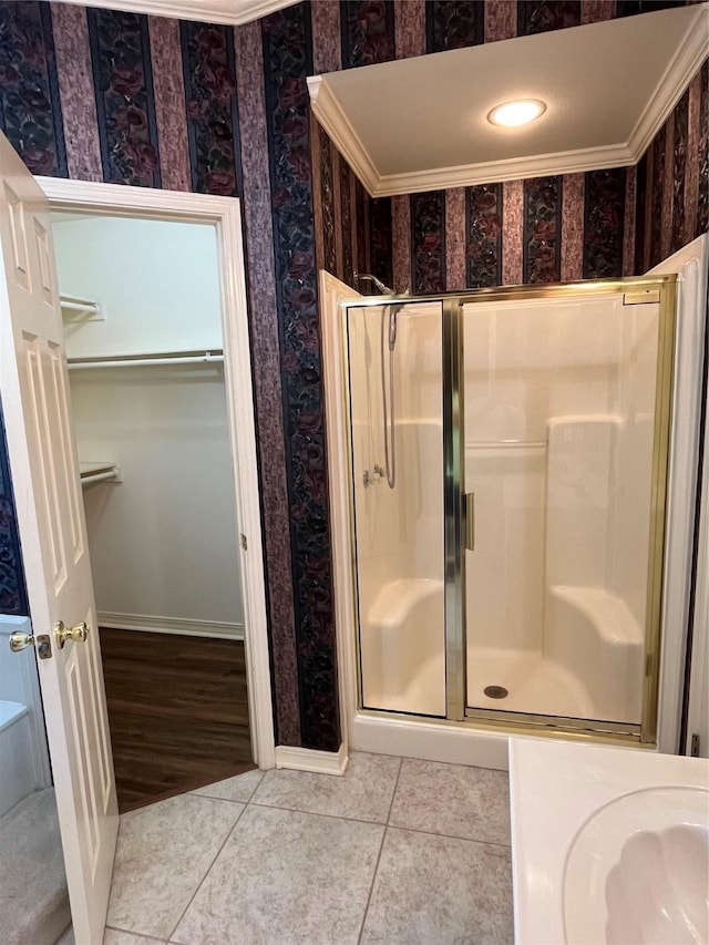 bathroom with wallpapered walls, a shower stall, a walk in closet, and tile patterned floors