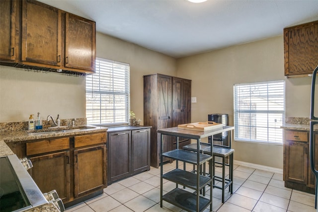 kitchen featuring a healthy amount of sunlight, light tile patterned floors, sink, and stone counters