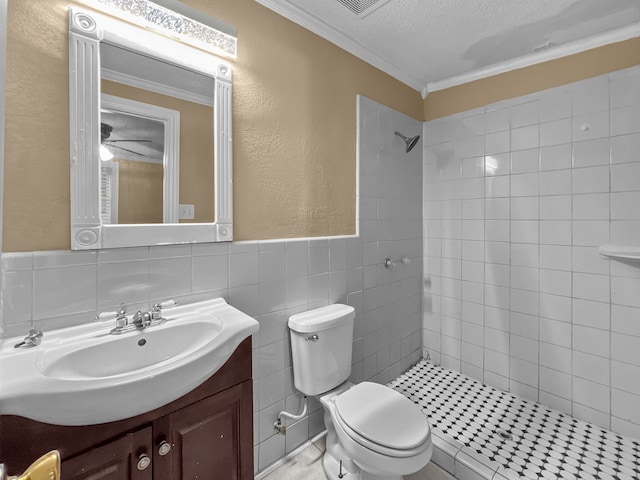 bathroom with a tile shower, crown molding, toilet, vanity, and tile walls