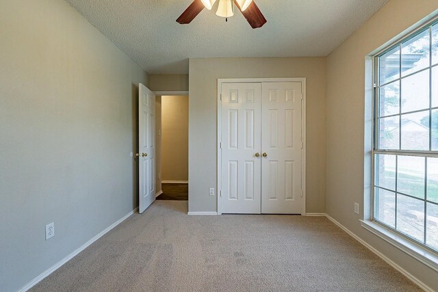 unfurnished bedroom featuring ceiling fan, light colored carpet, multiple windows, and a closet