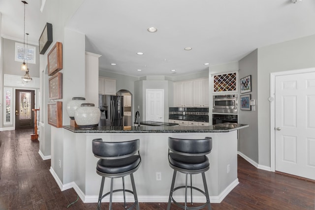 kitchen featuring hanging light fixtures, stainless steel fridge with ice dispenser, decorative backsplash, black oven, and white cabinetry