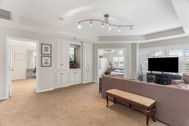 carpeted living room with a raised ceiling, ceiling fan, and a healthy amount of sunlight