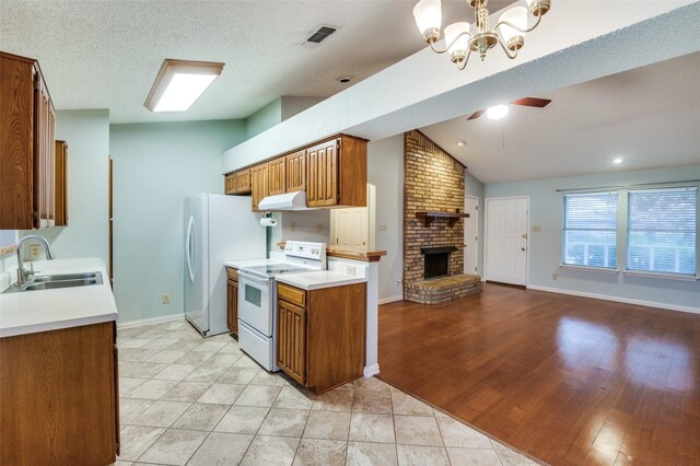 kitchen featuring lofted ceiling, white appliances, ceiling fan with notable chandelier, sink, and a brick fireplace