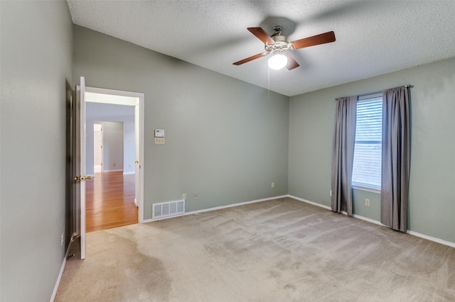 empty room featuring ceiling fan, light colored carpet, and a textured ceiling