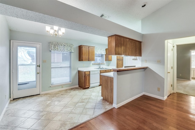 kitchen featuring sink, an inviting chandelier, kitchen peninsula, lofted ceiling, and white appliances