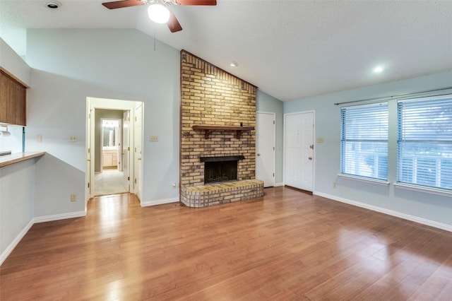 unfurnished living room featuring a textured ceiling, vaulted ceiling, ceiling fan, light hardwood / wood-style flooring, and a fireplace