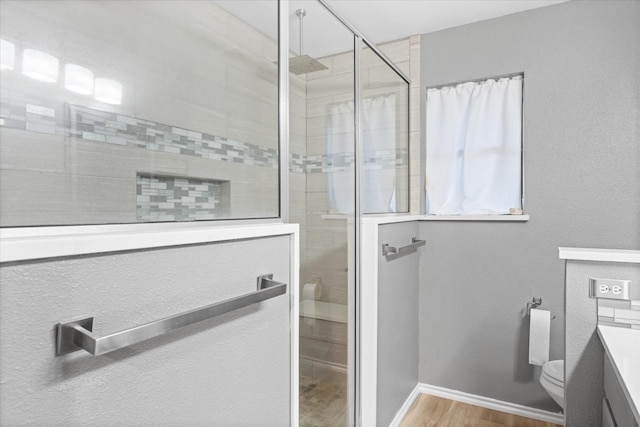 bathroom featuring a tile shower, hardwood / wood-style floors, vanity, and toilet