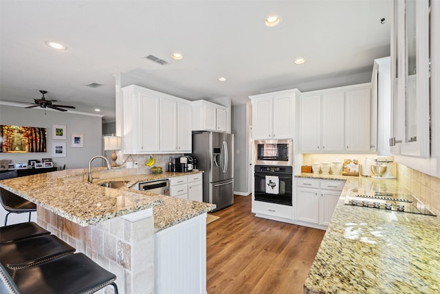 kitchen with kitchen peninsula, sink, black appliances, white cabinets, and a breakfast bar area