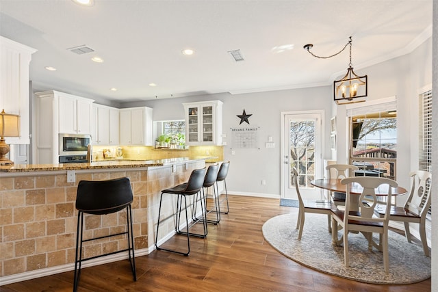 kitchen with backsplash, stainless steel microwave, white cabinets, and hanging light fixtures