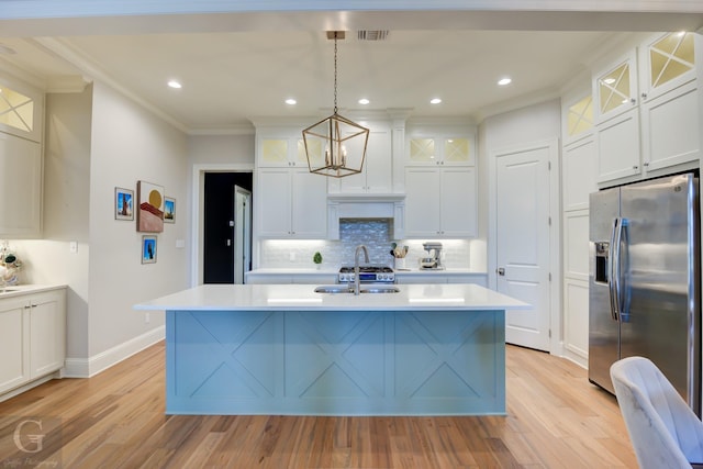 kitchen featuring sink, decorative light fixtures, ornamental molding, stainless steel fridge, and an island with sink