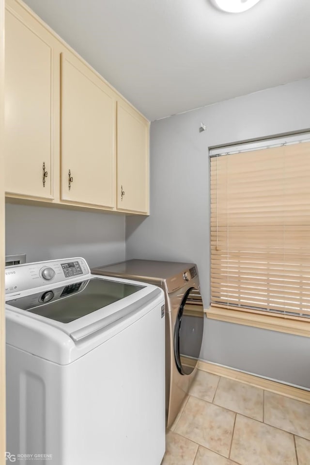 clothes washing area featuring cabinets, light tile patterned flooring, and washing machine and clothes dryer