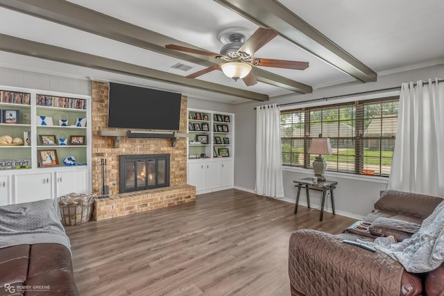 living room with built in shelves, ceiling fan, beam ceiling, hardwood / wood-style flooring, and a fireplace