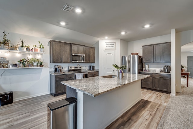 kitchen with sink, an island with sink, dark brown cabinets, and stainless steel appliances