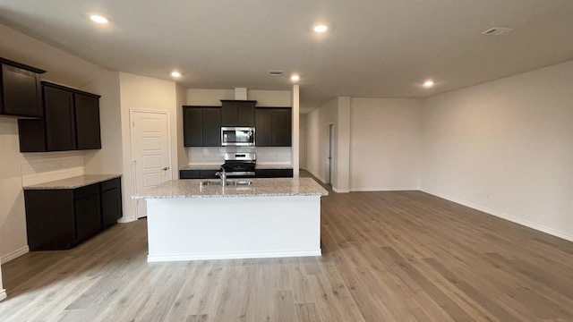 4219 Sky Dr, Sherman, TX 75090 - kitchen with appliances with stainless steel finishes, decorative backsplash, an island with sink, light stone counters, and light wood finished floors