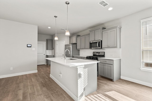 kitchen with a center island with sink, gray cabinetry, sink, and appliances with stainless steel finishes