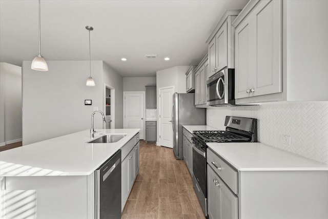 kitchen featuring a center island with sink, sink, hanging light fixtures, light hardwood / wood-style flooring, and stainless steel appliances