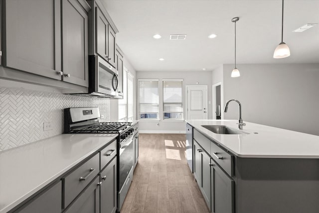 kitchen with appliances with stainless steel finishes, sink, pendant lighting, a center island with sink, and gray cabinets