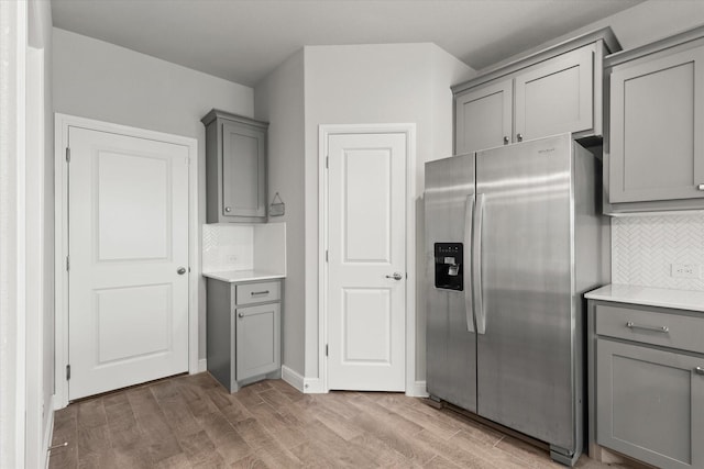 kitchen featuring stainless steel refrigerator with ice dispenser, backsplash, light hardwood / wood-style floors, and gray cabinetry