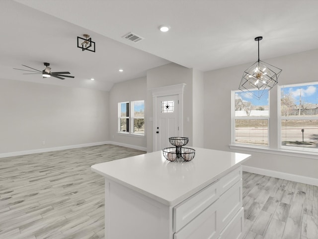 kitchen with ceiling fan with notable chandelier, white cabinets, hanging light fixtures, a center island, and light hardwood / wood-style flooring