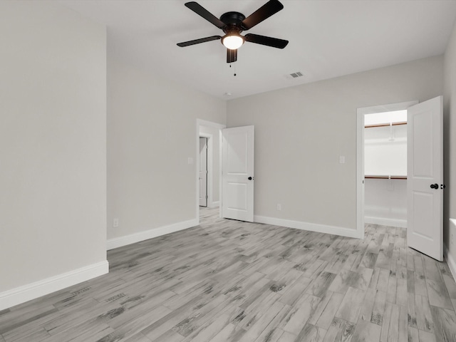 unfurnished bedroom with ceiling fan, a spacious closet, light wood-type flooring, and a closet