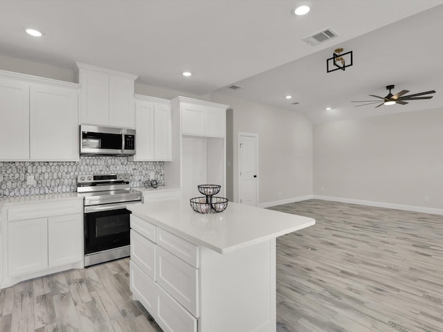 kitchen with appliances with stainless steel finishes, white cabinetry, decorative backsplash, a center island, and light hardwood / wood-style flooring