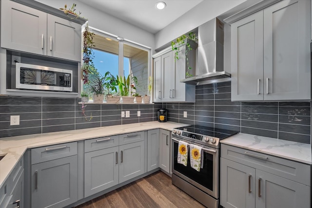 kitchen with light stone counters, wall chimney exhaust hood, stainless steel appliances, gray cabinets, and dark hardwood / wood-style floors