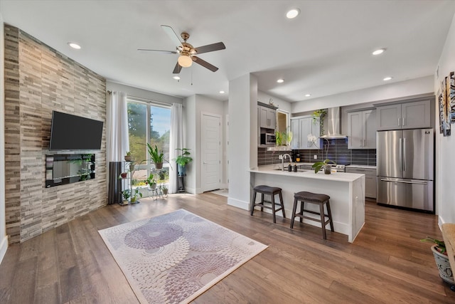 kitchen featuring gray cabinetry, wall chimney exhaust hood, stainless steel appliances, a kitchen bar, and hardwood / wood-style flooring