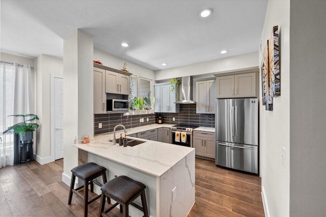 kitchen featuring appliances with stainless steel finishes, a kitchen breakfast bar, wall chimney exhaust hood, sink, and gray cabinets