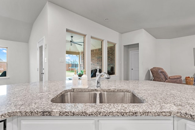 kitchen with light stone counters, white cabinetry, ceiling fan, and sink