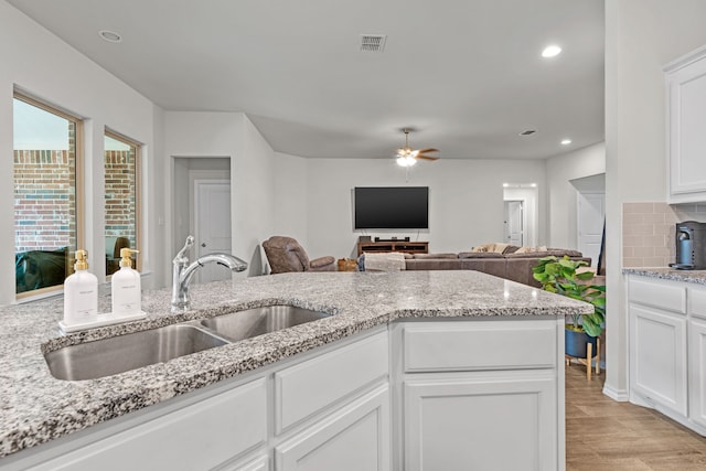 kitchen featuring backsplash, white cabinets, sink, ceiling fan, and light stone counters