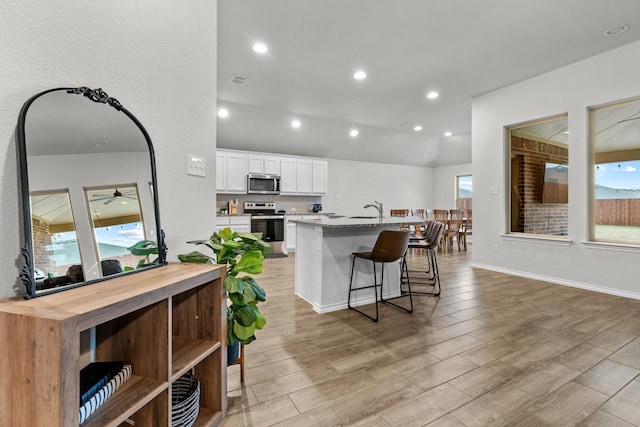 kitchen with a breakfast bar, a center island with sink, light stone countertops, appliances with stainless steel finishes, and white cabinetry