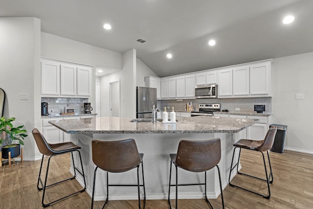 kitchen with a kitchen island with sink, white cabinets, a kitchen breakfast bar, light stone counters, and stainless steel appliances